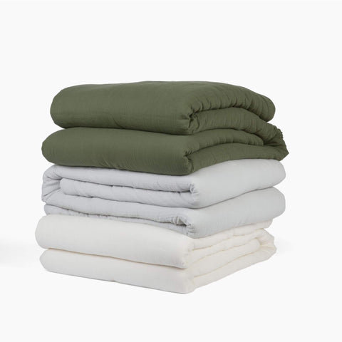 Avec cotton quilts in various colors stacked neatly on a white background