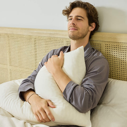 A young man sitting in his bed made with Avec bedding and clutching his pillow